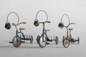 Three original 1960s tricycles — one red, one blue, and one green — transformed into traveling libraries with adjustable reading lamps