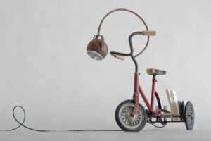 Front view of Gino, an authentic 1940s Italian iron tricycle with a wooden seat and pedals, transformed into a traveling lamp and bookshelf