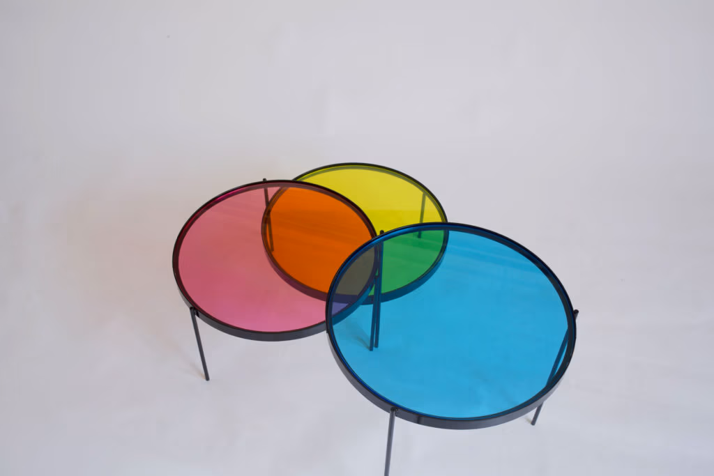 CMYK coffee table by Manoteca, rotation sequence 05: cyan disc shifted far left, triple overlap at centre generating a near-black intersection, cyan-magenta overlap producing a blue-violet area, magenta and yellow discs stationary.