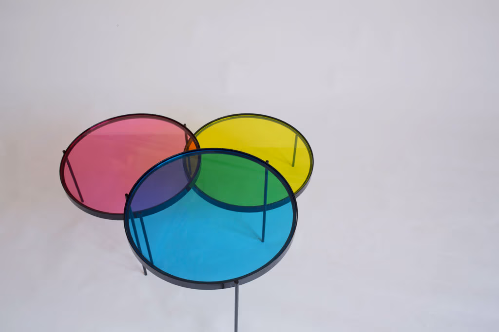 CMYK coffee table by Manoteca, rotation sequence 09: magenta disc continuing downward, cyan and yellow discs stationary, violet cyan-magenta overlap prominent, orange magenta-yellow intersection nearly dissolved.