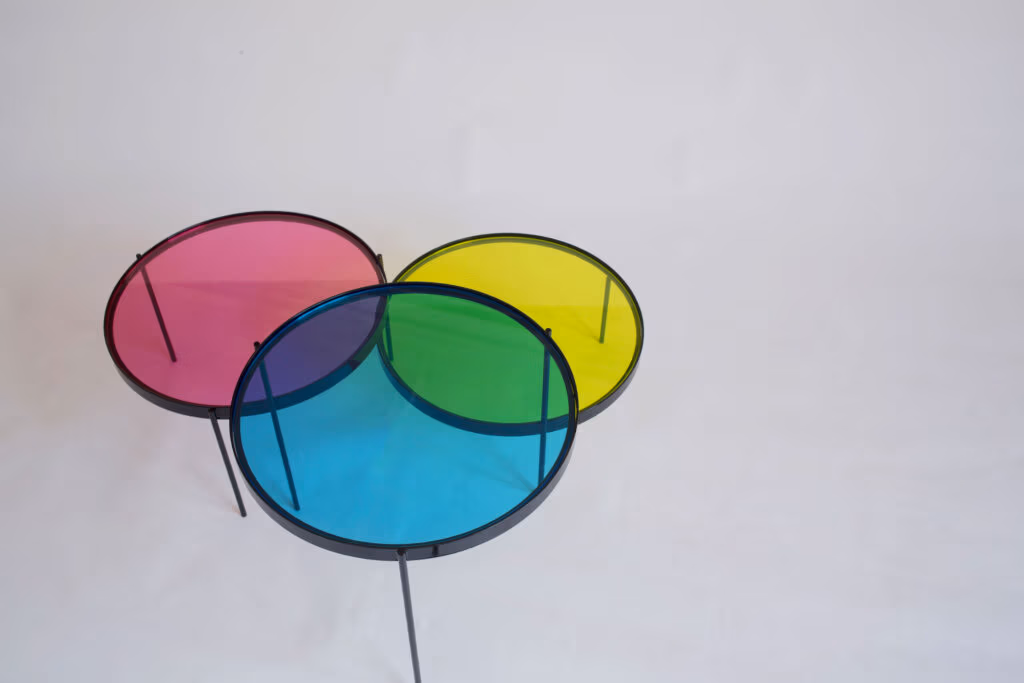 CMYK coffee table by Manoteca, rotation sequence 10: magenta disc rotated far downward, cyan and yellow discs stationary, green cyan-yellow overlap dominant, violet cyan-magenta intersection visible, magenta fully separated from yellow.
