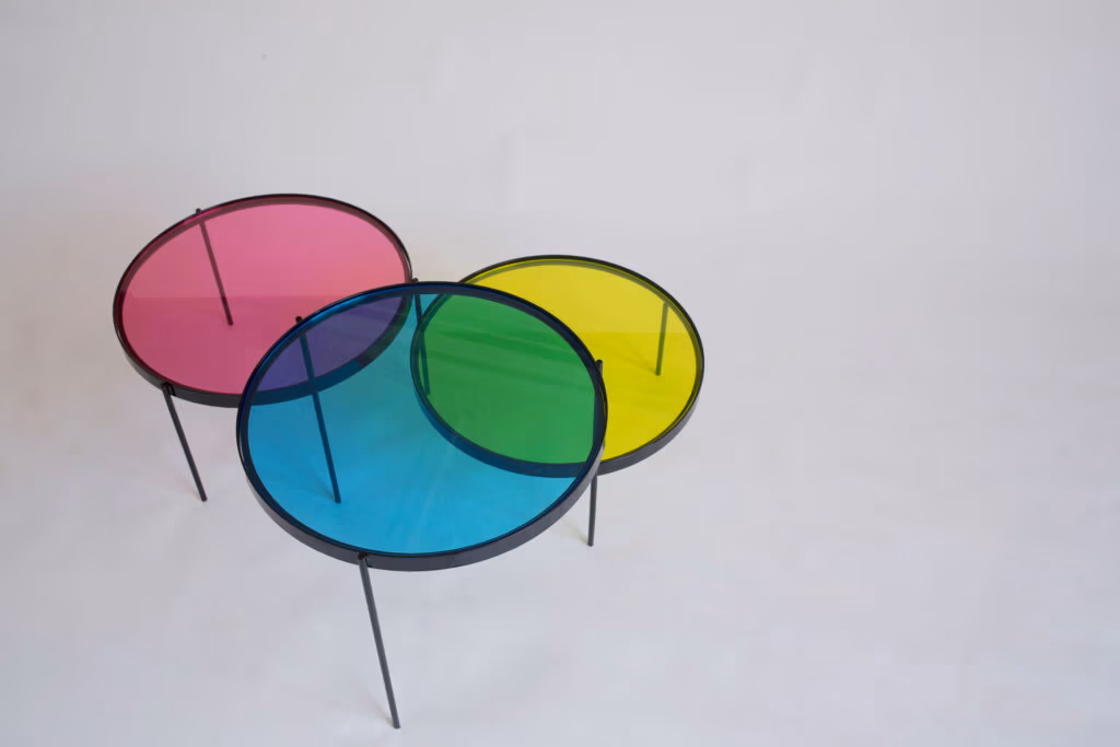 CMYK coffee table by Manoteca, rotation sequence 11: magenta disc rotating further right, cyan and yellow discs stationary, green cyan-yellow overlap dominant at centre, violet cyan-magenta intersection reducing.