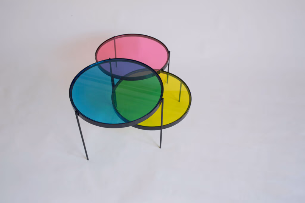 CMYK coffee table by Manoteca, rotation sequence 16: magenta disc shifting left, cyan and yellow discs stationary, green cyan-yellow overlap persisting, violet cyan-magenta intersection reappearing at upper left.