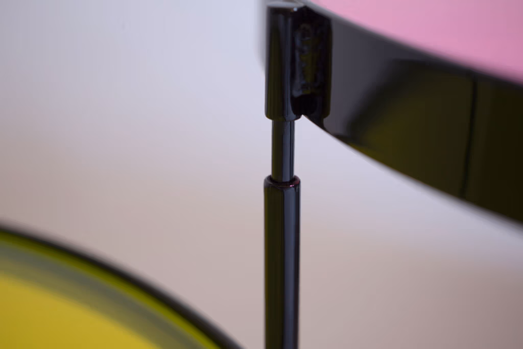 CMYK coffee table by Manoteca, assembly sequence 04: close-up of black metal male leg nearly fully inserted into female socket, yellow and magenta glass discs visible in background.