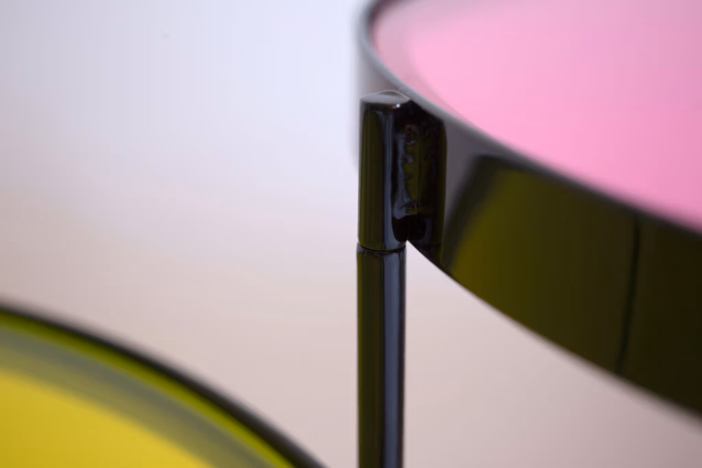 CMYK coffee table by Manoteca, assembly sequence 05: black metal rotating pin joint fully assembled, magenta glass disc visible in background, structural hinge detail complete.